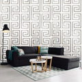 Modern living room with a black sectional sofa, patterned rug, and geometric wall design.