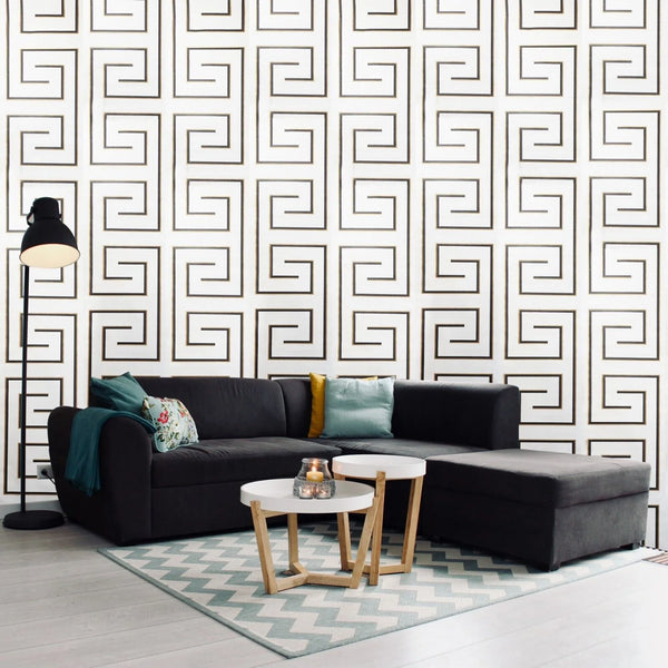 Modern living room with a black sectional sofa, patterned rug, and geometric wall design.