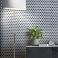 Room interior with geometric patterned wallpaper, lamp, plant, and table.