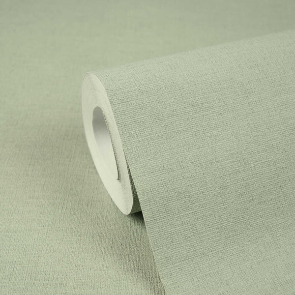 AS Creation Cosiness 792431 close up of a soft green textured wallpaper roll, partially unrolled on a matching surface.