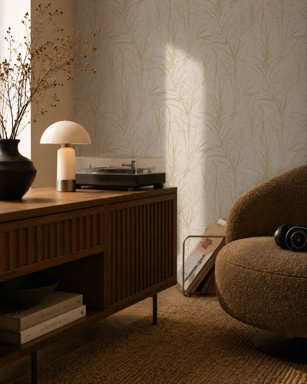 AS Creation Cosiness 792823 living room with botanical grass motif wallpaper in Brown, Cream, Metallic, shown behind a wooden sideboard and a rounded lounge chair.