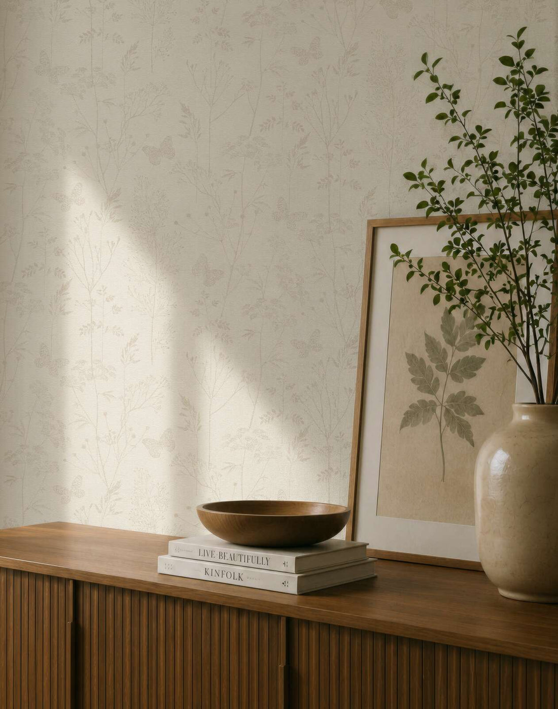 AS Creation Cosiness 792831 beige and brown wallpaper with a delicate botanical and butterfly pattern behind a wooden cabinet with a framed leaf print and a ceramic vase with branches.