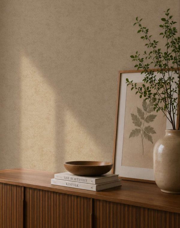 AS Creation Cosiness 792841 softly mottled wallpaper behind a wood sideboard styled with a framed botanical print, a ceramic vase with greenery, and a wooden bowl on stacked books.