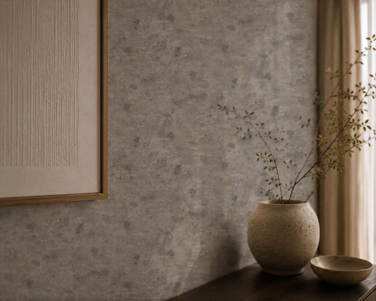 AS Creation Cosiness 793181 brown, Grey, Metallic mottled wallpaper with irregular speckling; a framed artwork hangs above a dark surface holding a ceramic vase with branches and a small bowl beside a light curtain.