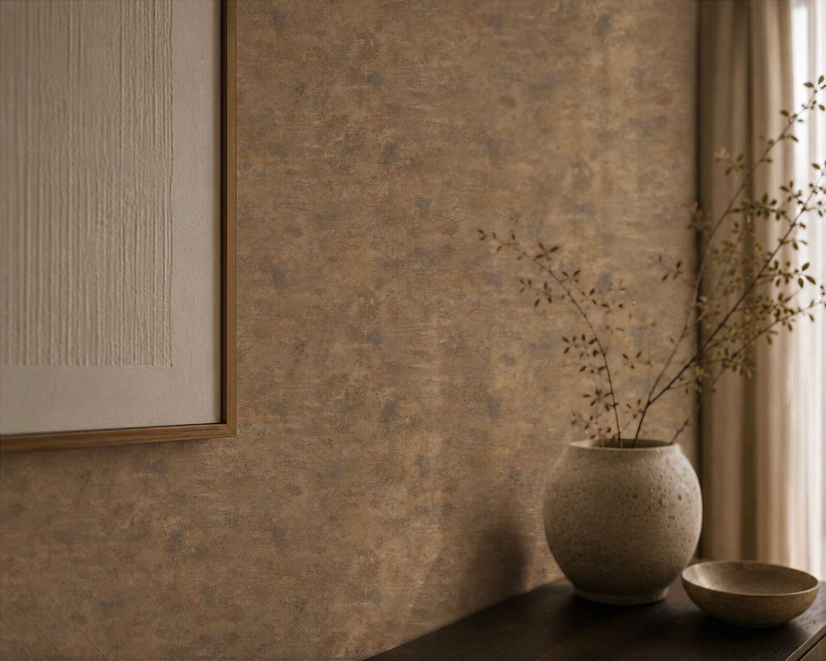 AS Creation Cosiness 793182 brown wallpaper with a mottled look and subtle metallic and orange tones, shown behind a framed textured artwork, a ceramic vase with twigs, a small bowl, and a curtain.