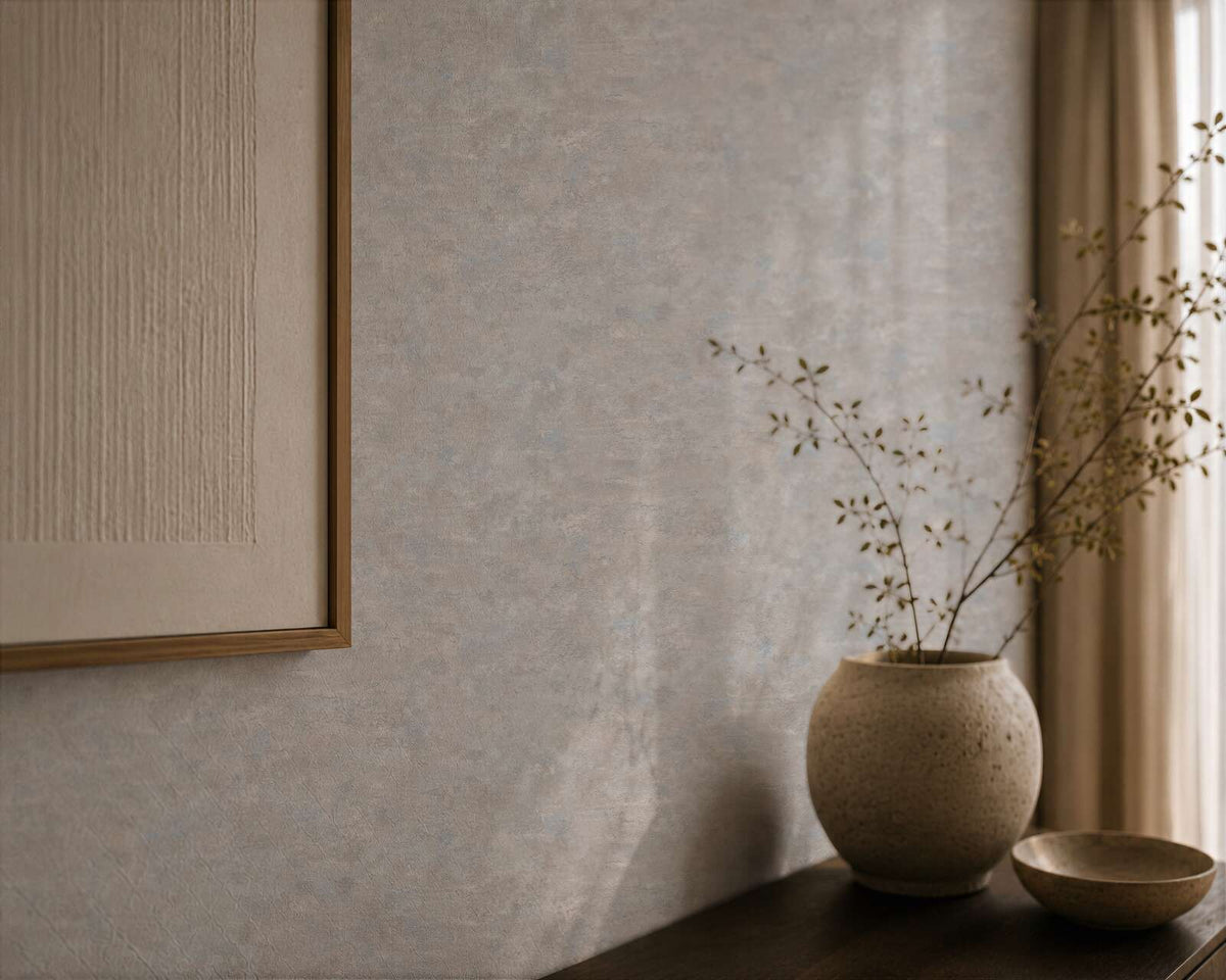 AS Creation Cosiness 793185 grey, Metallic wallpaper with a subtle mottled texture, shown with a ceramic vase holding branches on a console, a small bowl, a framed artwork, and a curtain.