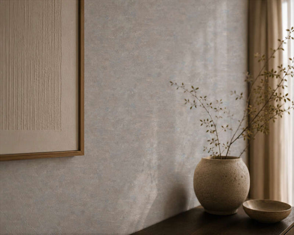 AS Creation Cosiness 793185 grey, Metallic wallpaper with a subtle mottled texture, shown with a ceramic vase holding branches on a console, a small bowl, a framed artwork, and a curtain.