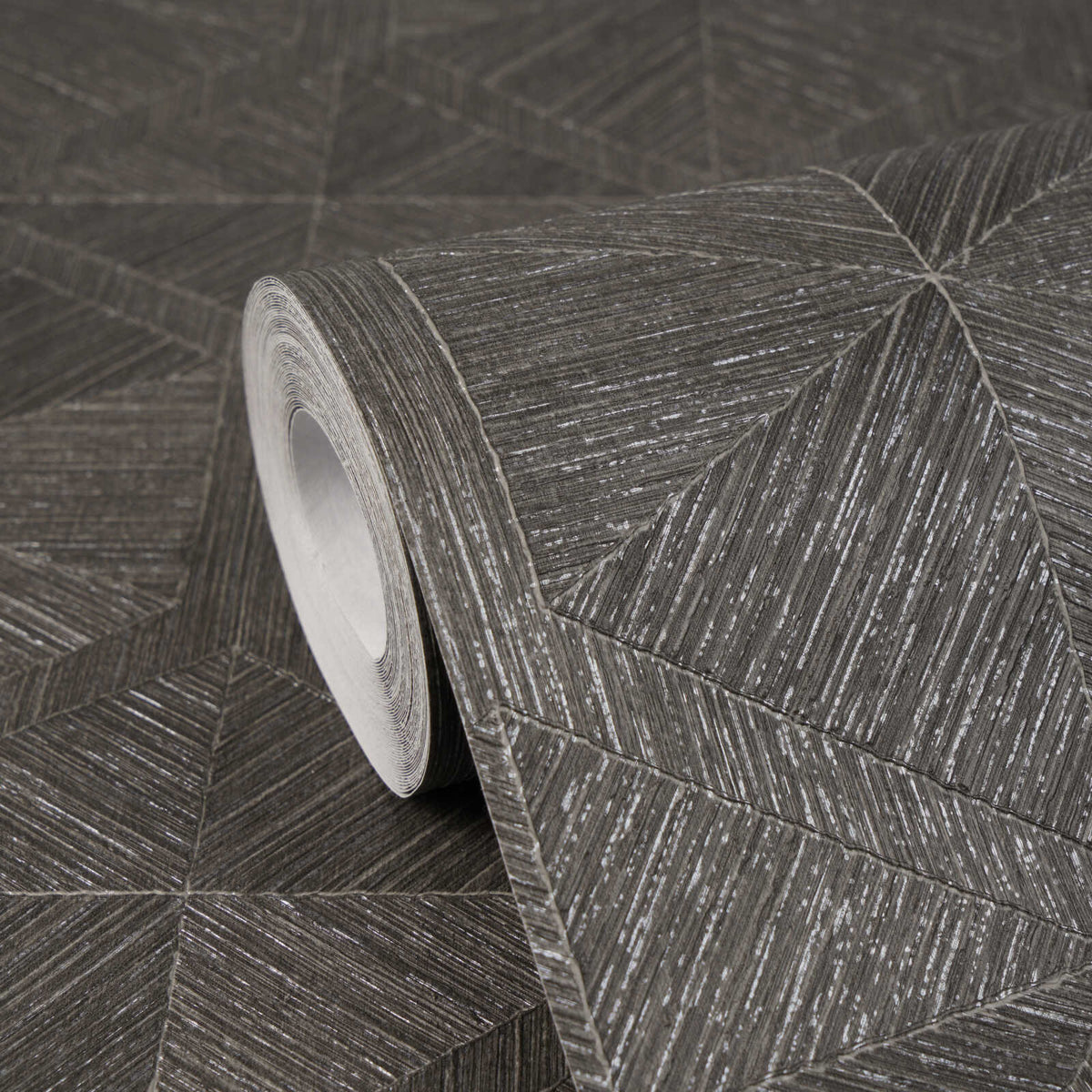 AS Creation Cosiness 793196 close up of a wallpaper roll on matching unrolled, showing a geometric pattern of angled lines forming triangles and diamonds in Brown, Grey, Metallic.