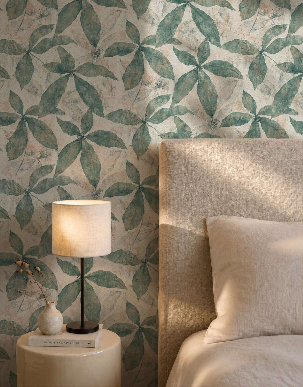 AS Creation Cosiness 793201 large green leafy motif arranged in clusters on a beige and cream ground with a painterly, weathered wallpaper on a bedroom feature wall.