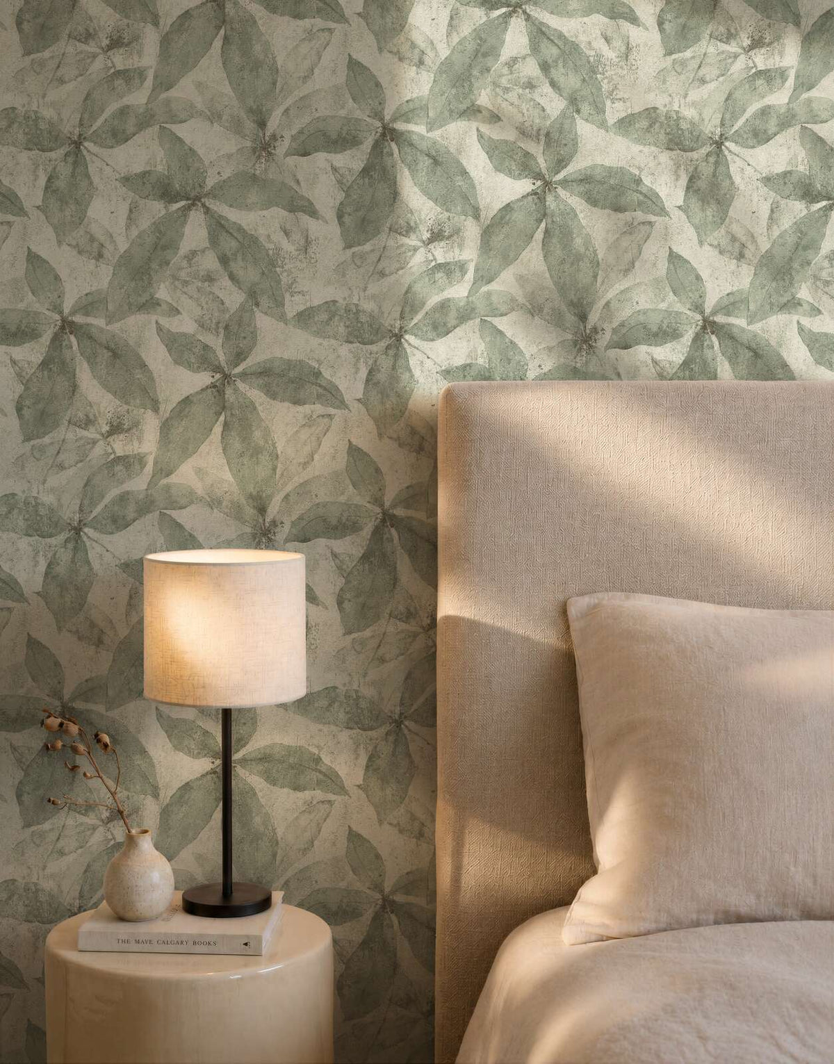 AS Creation Cosiness 793202 bedroom with Cream and Green leaf wallpaper behind a bed and a table lamp.
