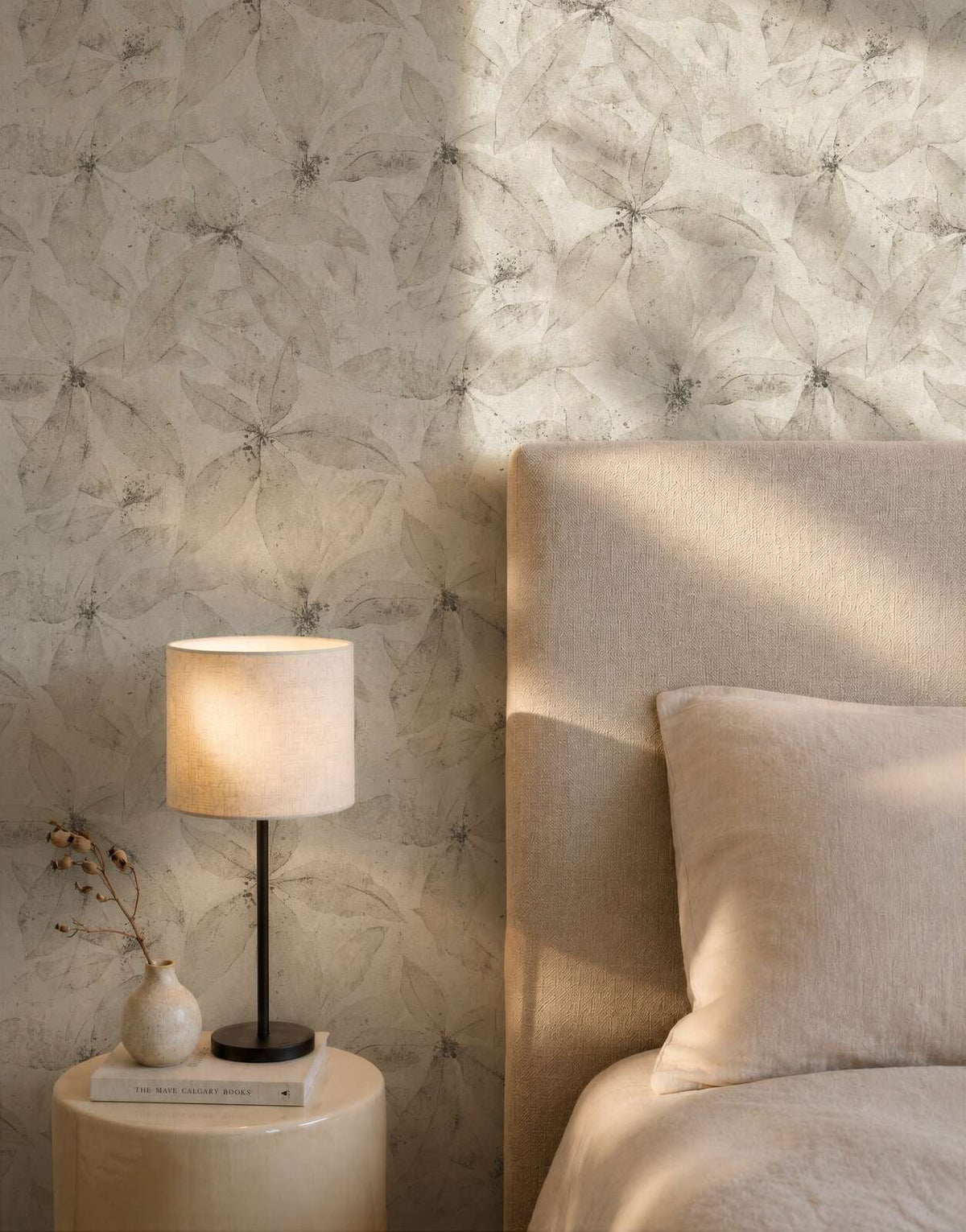 AS Creation Cosiness 793204 bedroom with beige and cream floral wallpaper behind a bed and a table lamp.