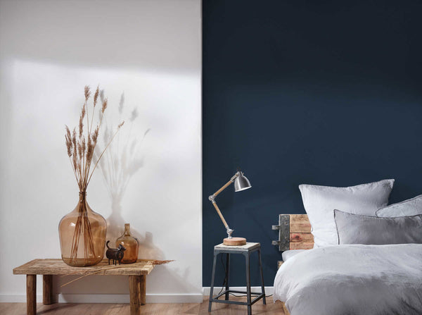 AS Creation French Affair 356536 bedroom with Blue solid wallpaper on a feature wall beside a bed and a table lamp.