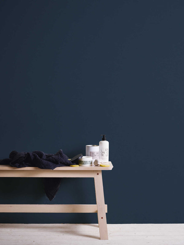 AS Creation French Affair 356536 blue wallpaper behind a light wood bench with a dark towel, pump bottle, and small jars.