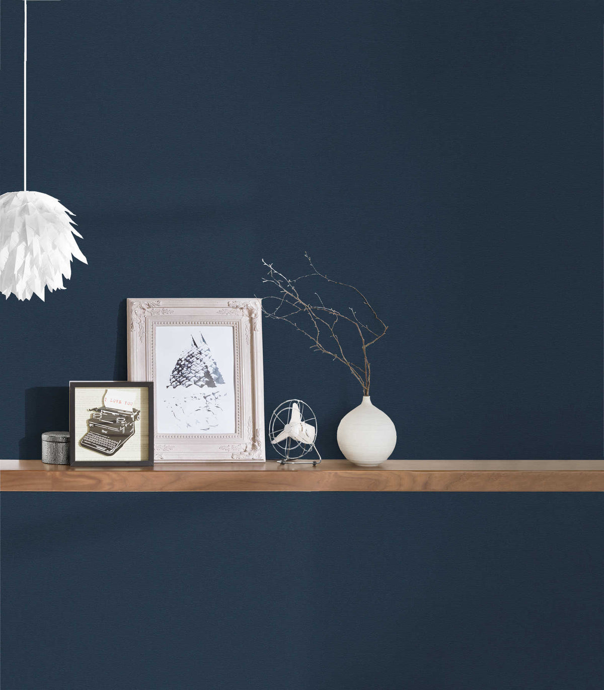 AS Creation French Affair 356536 blue wallpaper behind a floating wood shelf with framed art and a small white vase, plus a white pendant light at the side.