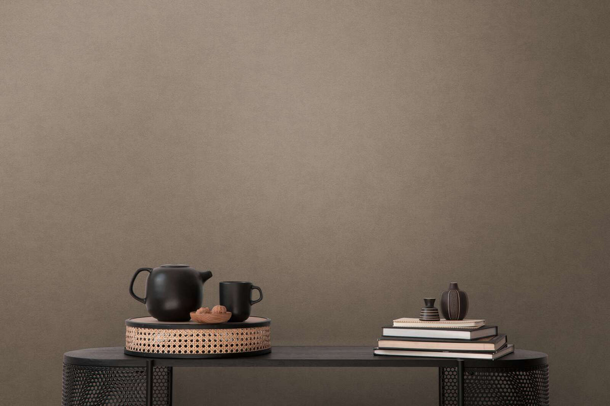 AS Creation French Affair 393419 brown wallpaper with a subtle textured look behind a console table styled with a black teapot, mug, stacked books, and two small vases.