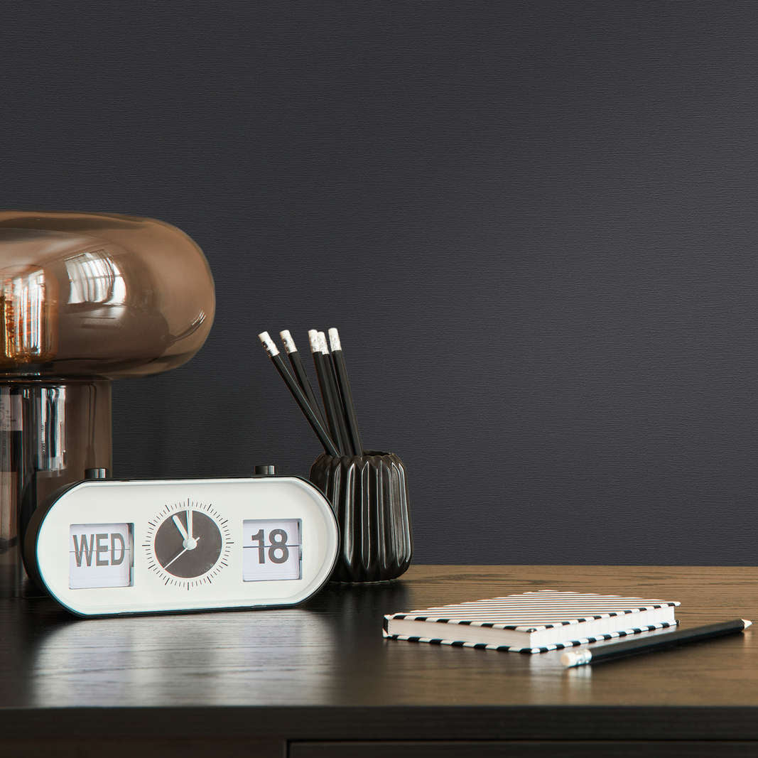 AS Creation French Affair 395726 black wallpaper behind a desk with a flip clock, pencil cup, and notebook.
