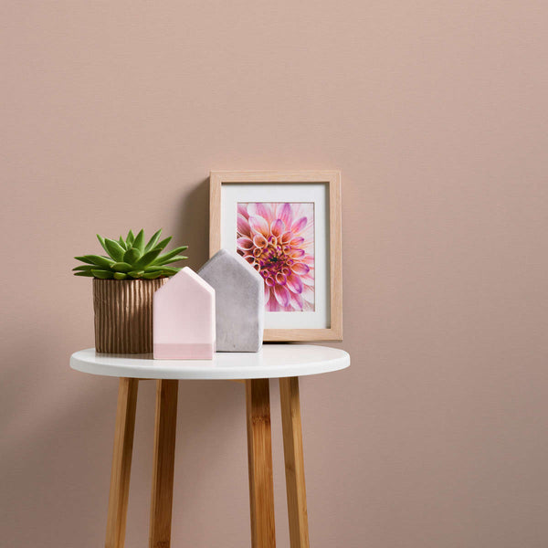 AS Creation French Affair 395757 beige, Cream wallpaper behind a small round side table styled with a potted succulent, two small house shaped ornaments, and a framed flower print.