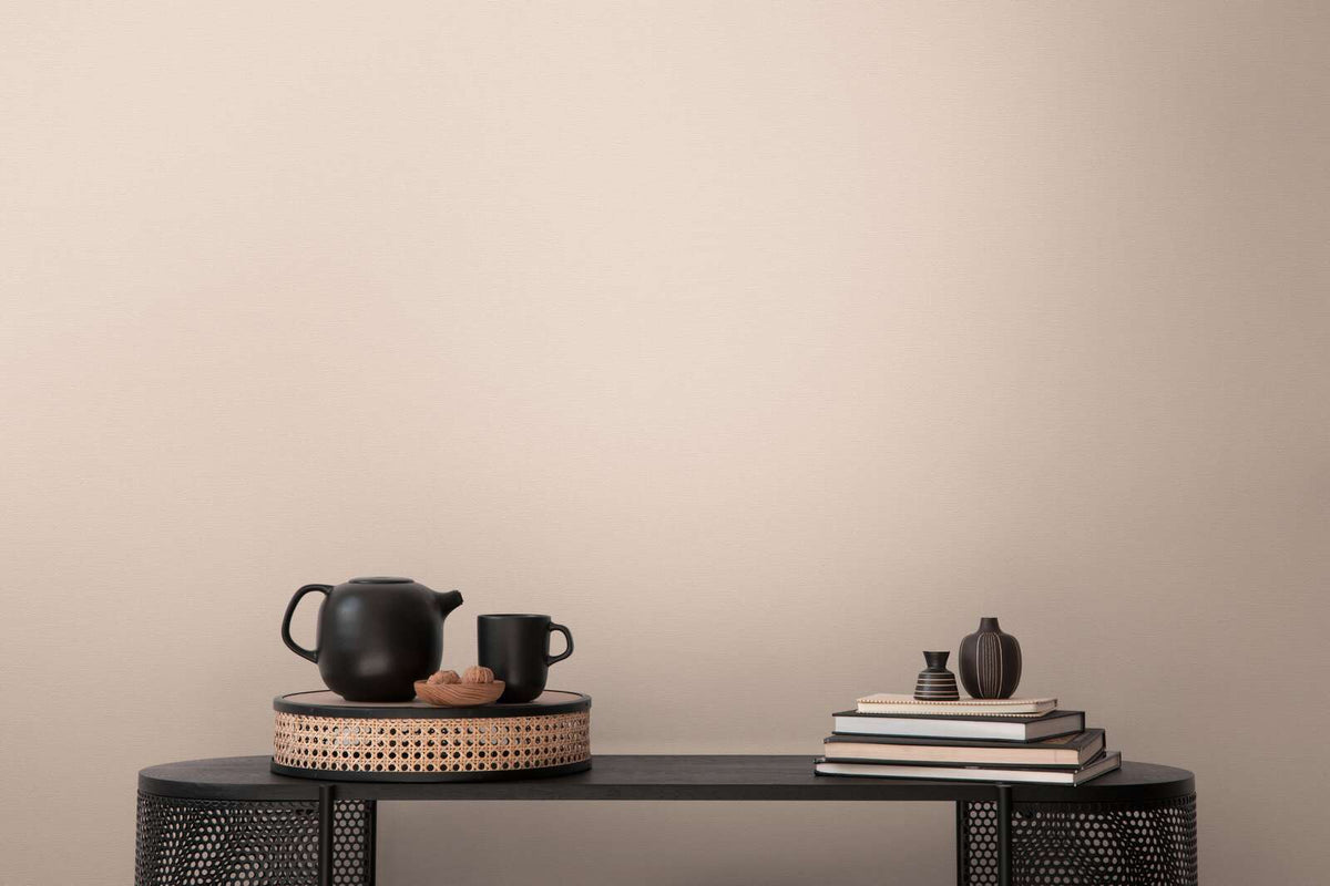 AS Creation French Affair 395757 beige and cream textured wallpaper behind a black console styled with a teapot, mug, stacked books, and two small vases.