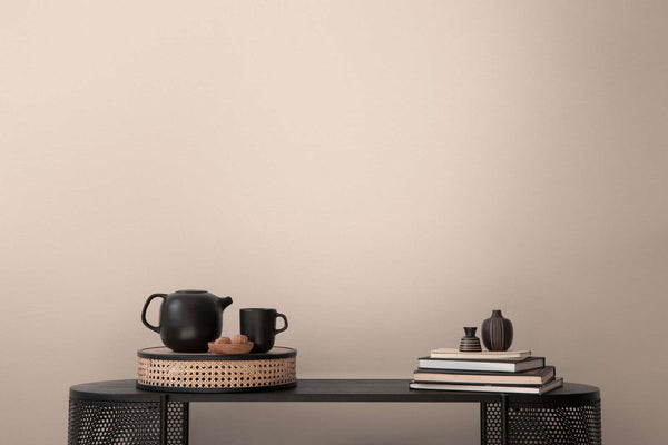 AS Creation French Affair 395757 beige and cream textured wallpaper behind a black console styled with a teapot, mug, stacked books, and two small vases.