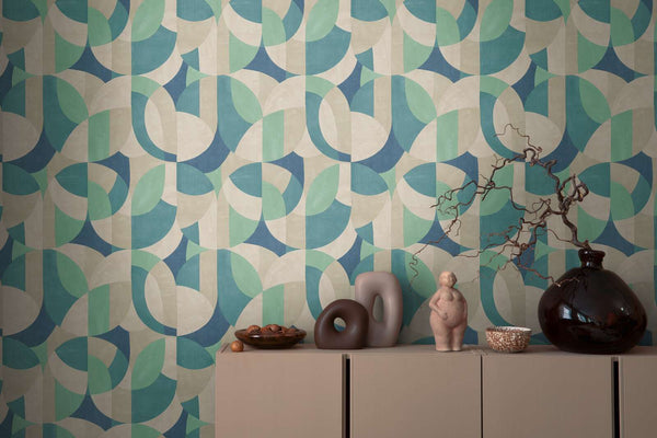 AS Creation French Affair 399322 abstract geometric wallpaper in Beige, Blue, Cream, Green, and Turquoise behind a console with a dark glass vase holding a branch and sculptural ceramics.