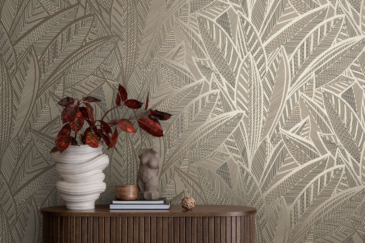 AS Creation French Affair 399332 abstract leaf motif wallpaper in Black, Gold, Metallic behind a wood console with a sculptural white vase holding red leaves and a small torso sculpture on books.