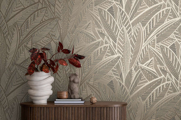 AS Creation French Affair 399332 abstract leaf motif wallpaper in Black, Gold, Metallic behind a wood console with a sculptural white vase holding red leaves and a small torso sculpture on books.