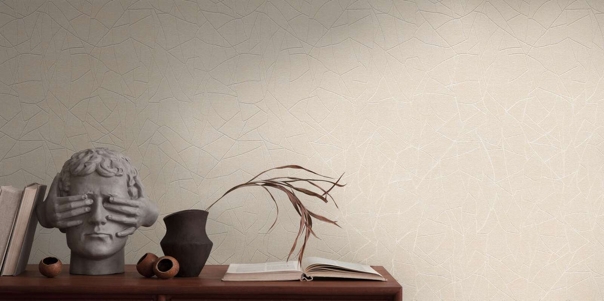 AS Creation French Affair 399342 beige, Cream, and White wallpaper with an abstract shard like line pattern behind a wooden console styled with a sculptural bust and a dark ceramic vase holding dried stems.
