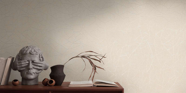 AS Creation French Affair 399342 beige, Cream, and White wallpaper with an abstract shard like line pattern behind a wooden console styled with a sculptural bust and a dark ceramic vase holding dried stems.
