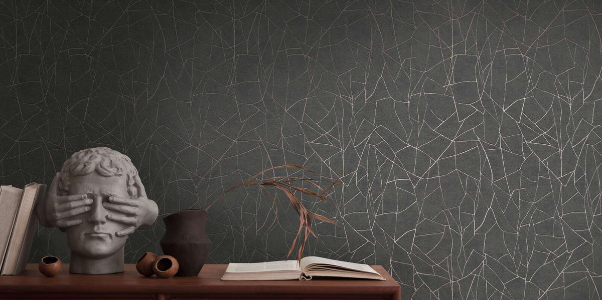 AS Creation French Affair 399344 abstract metallic gold line wallpaper on black with a console styled with a head sculpture, books, a vase with dried leaves, and an open book.