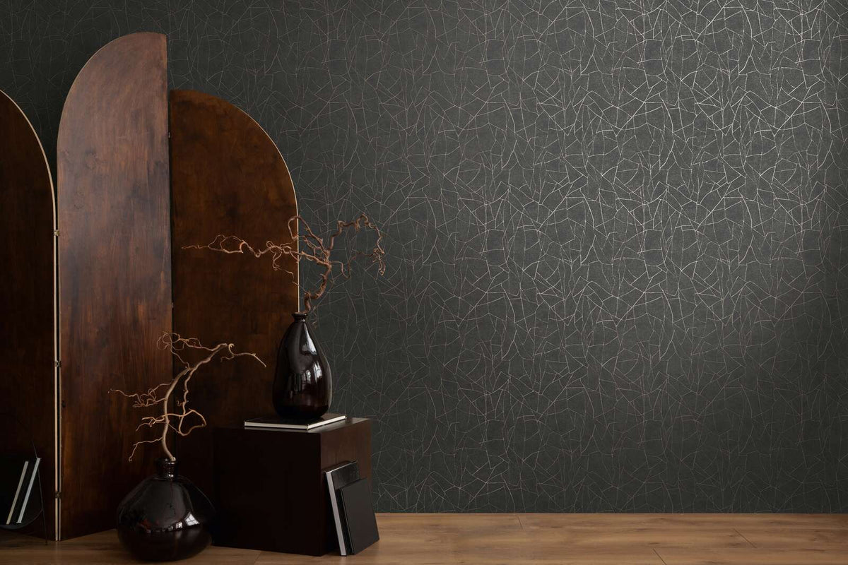 AS Creation French Affair 399344 black wallpaper with metallic gold linework in an abstract web pattern, styled with a wooden screen and two dark vases with branches on a wood floor.