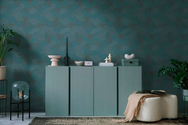 AS Creation French Affair 399353 living room scene featuring abstract curved pattern wallpaper in Black, Blue, Green, Turquoise behind a low cabinet; an ottoman sits in front.