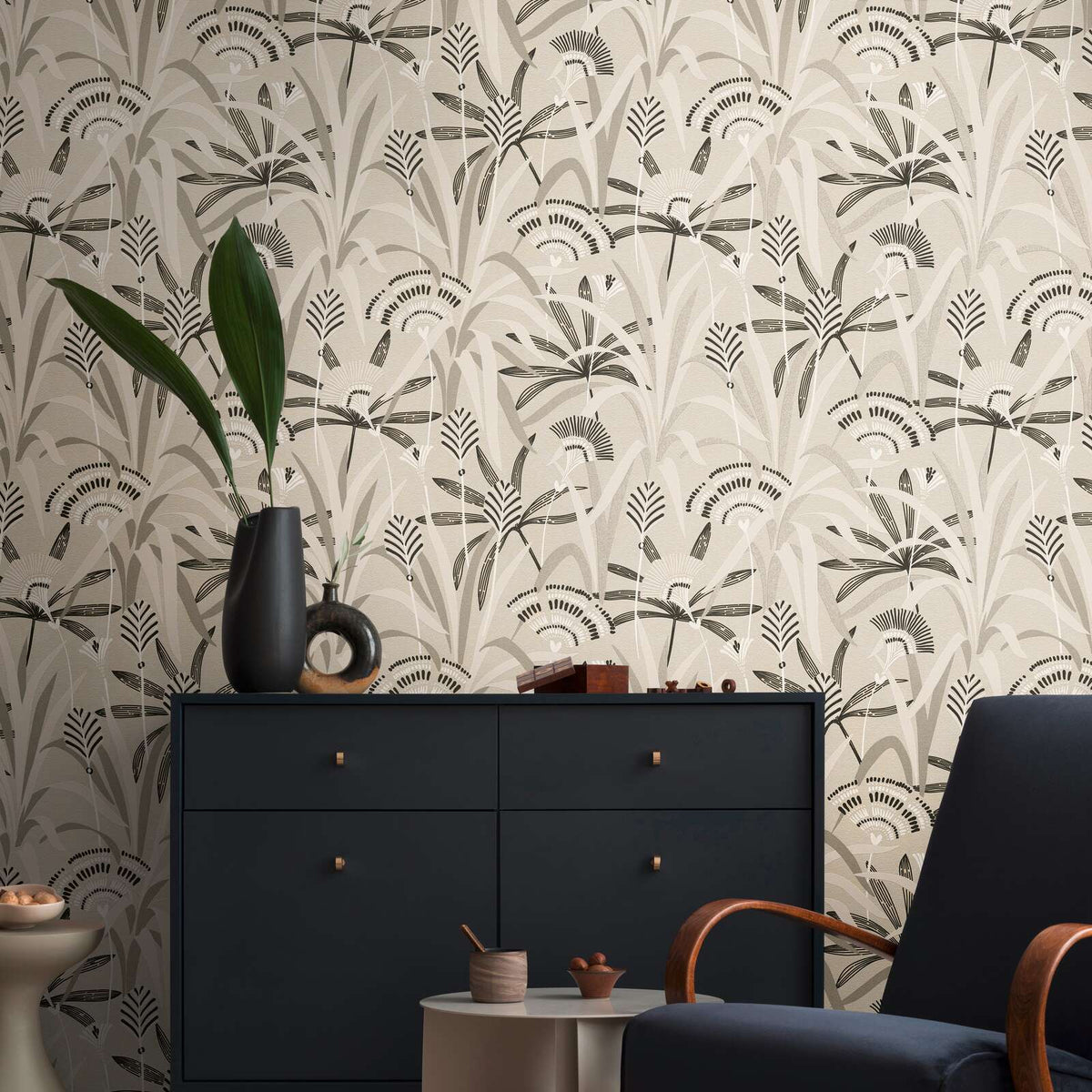 AS Creation French Affair 399361 living room with botanical wallpaper in Beige, Black, Grey, Taupe, and White, shown behind a dark sideboard and an armchair.