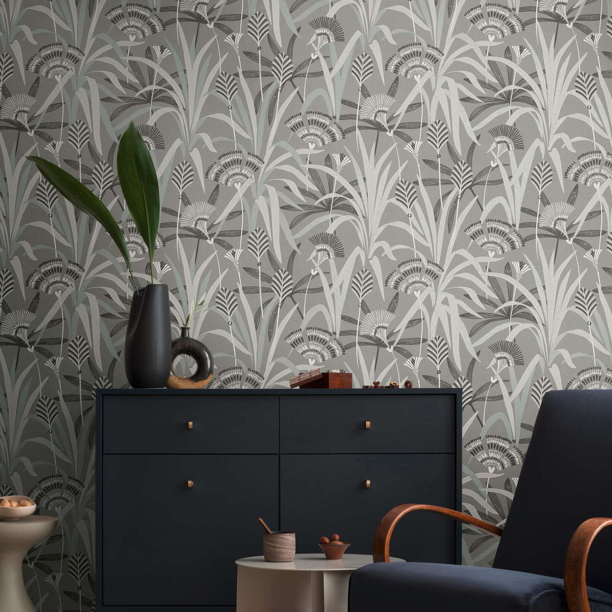 AS Creation French Affair 399362 living room with stylized botanical wallpaper in Black, Grey, Turquoise, and White, shown behind a dark sideboard and an armchair.