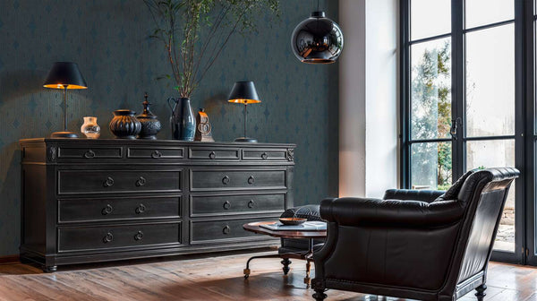 AS Creation French Affair 399373 living room with geometric Art Deco wallpaper in Beige, Blue, Gold, Green, Turquoise, shown with a dark dresser and a leather armchair.