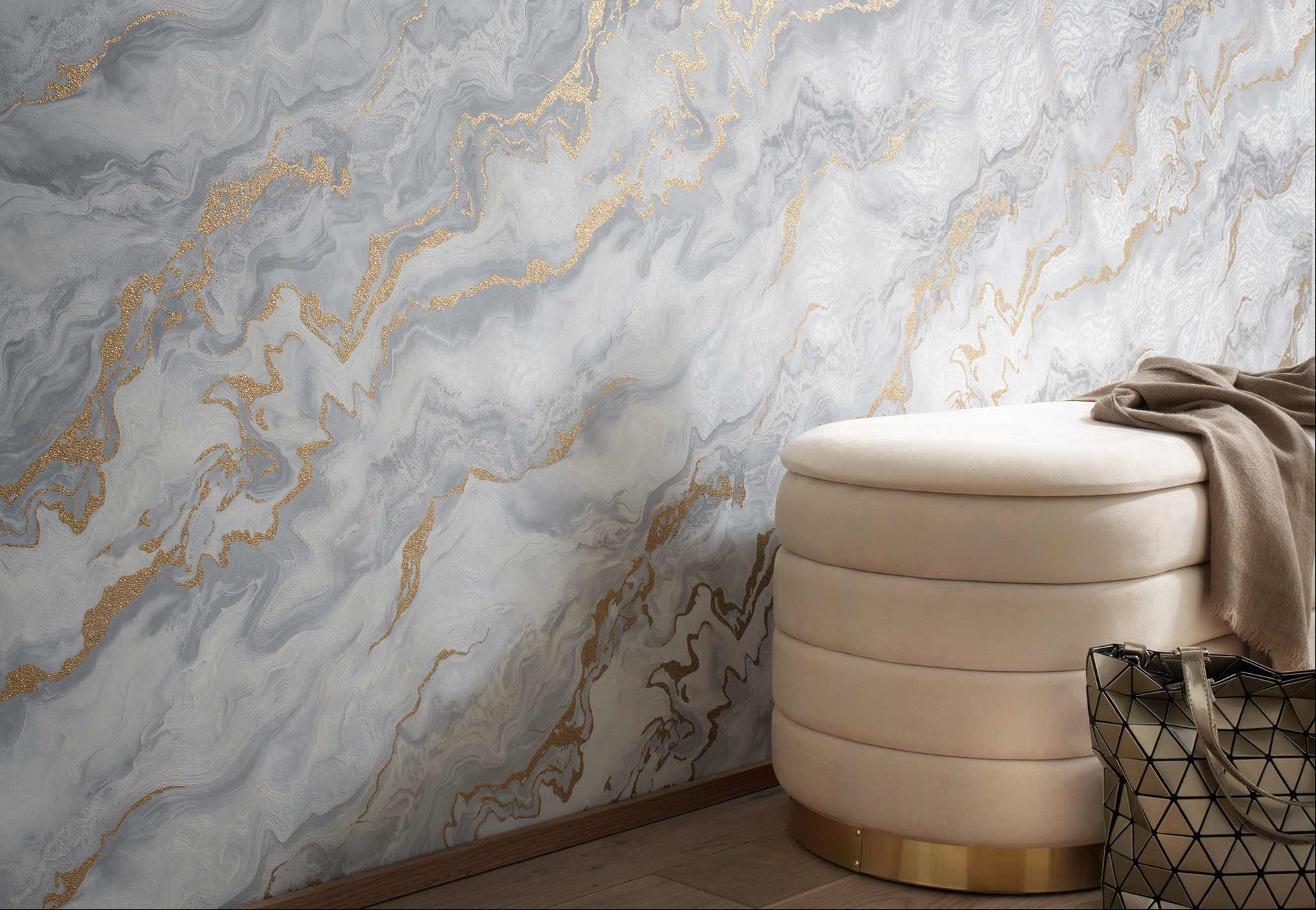 Erismann Elle Decoration 4 marble effect wallpaper in soft grey tones with gold accents styled in a modern interior with upholstered ottoman