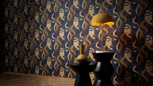 Erismann Elle Decoration abstract face wallpaper in navy blue and gold tones styled with decorative tables and a modern lamp in an interior setting