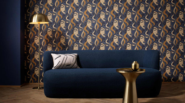 Erismann Elle Decoration abstract face wallpaper in navy blue and gold tones styled with a sofa and brass lighting in a modern interior