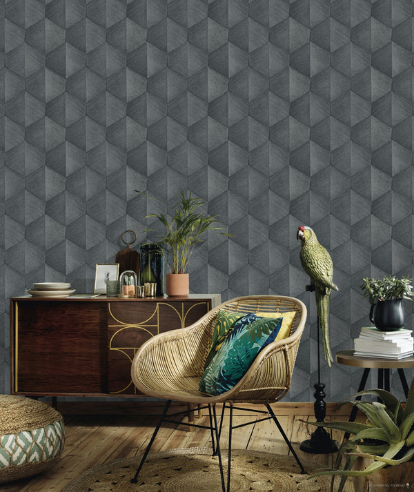 Erismann Fashion For Walls 4 10370-10 wallpaper lounge feature wall with a grey 3D geometric pattern behind a rattan chair with patterned cushions, a wooden sideboard, potted plants, and a relaxed tropical vibe.