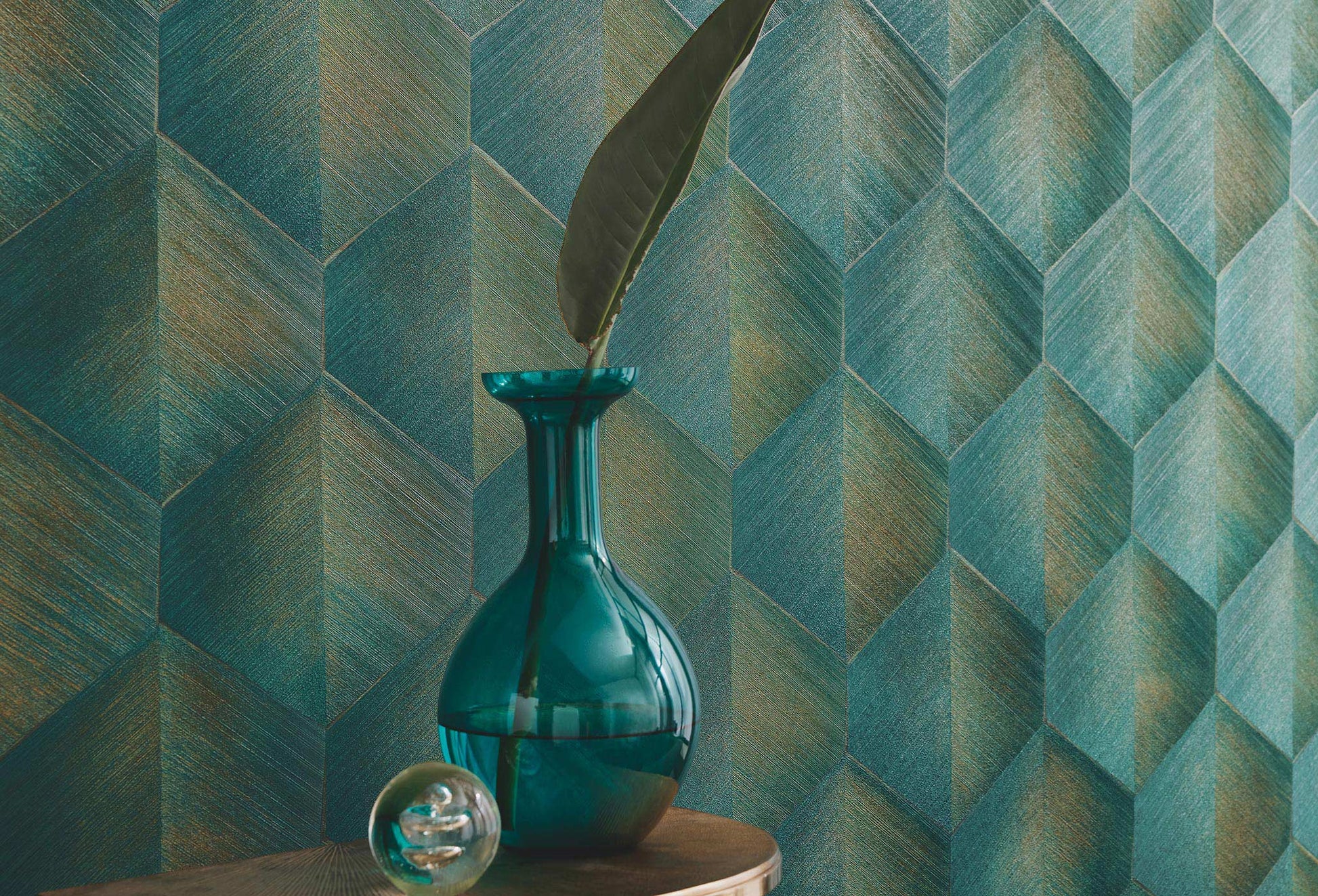 Erismann Fashion For Walls 4 10370-19 wallpaper lounge feature wall with teal geometric pattern, round side table, teal glass vase with a single leaf and a glass orb, calm modern mood.