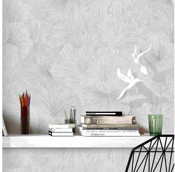 Erismann Fashion For Walls 4 10373-31 wallpaper lounge feature wall with subtle leaf pattern, a floating shelf styled with books and pencil pots, a glass tumbler and a modern wire chair, calm minimalist vibe.