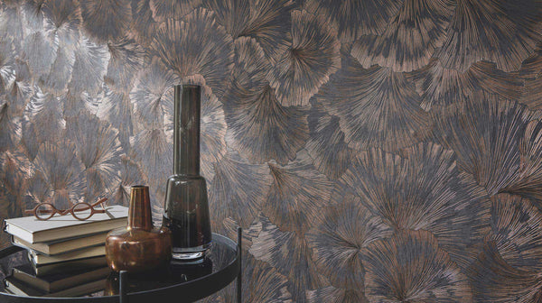 Erismann Fashion For Walls 4 10373-47 wallpaper lounge feature wall with dark metallic botanical pattern behind a round side table holding stacked books, glasses, and vases for a moody, sophisticated feel.