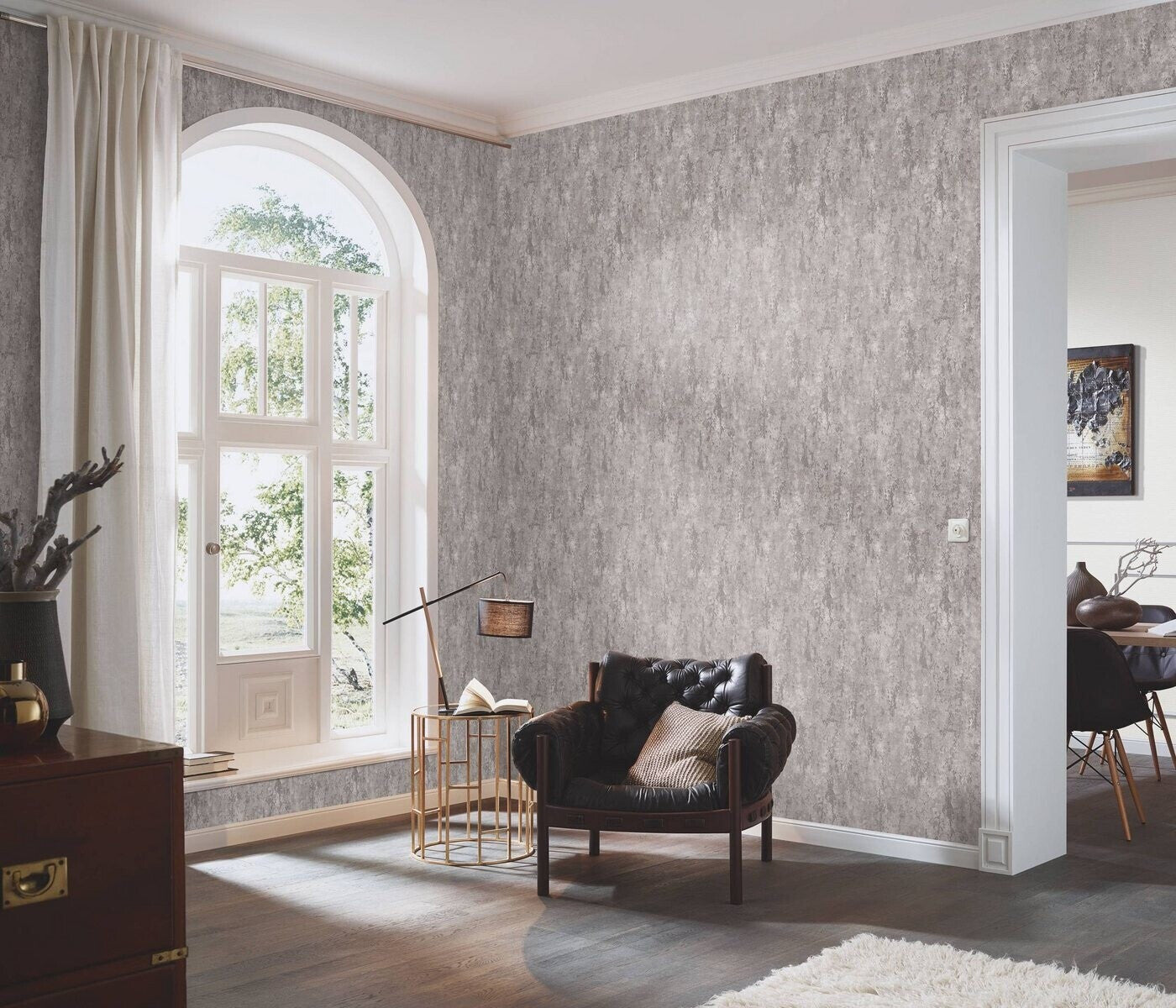 Erismann Fashion For Walls 4 10375-38 wallpaper feature wall in a bright lounge with arched window and curtains, tufted armchair, round side table with lamp and book, soft rug, and minimal decor.