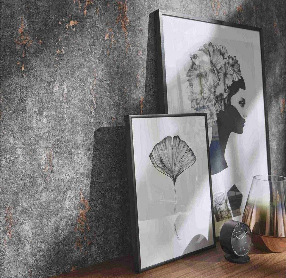 Erismann Fashion For Walls 4 10375-47 wallpaper lounge feature wall with distressed industrial texture, wooden console surface, leaning framed prints, small clock and glass vase for a moody modern look.