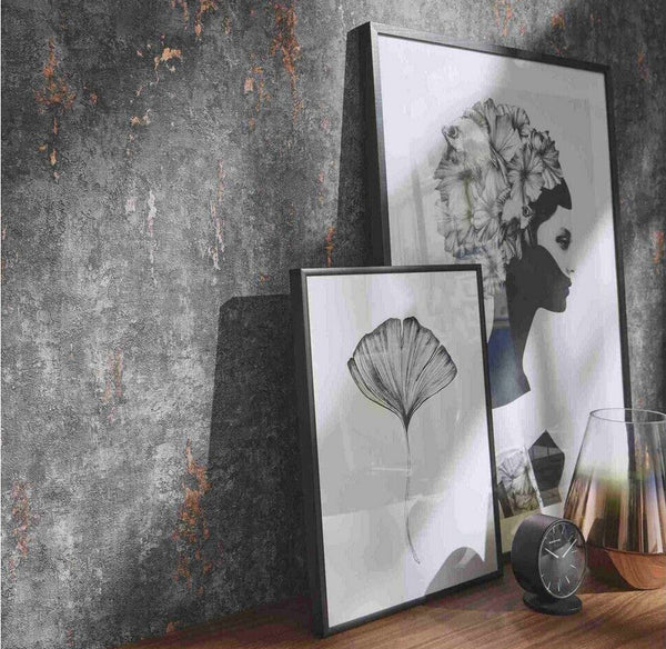 Erismann Fashion For Walls 4 10375-47 wallpaper lounge feature wall with distressed industrial texture, wooden console surface, leaning framed prints, small clock and glass vase for a moody modern look.
