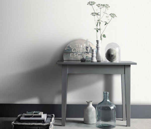 Erismann Fashion For Walls 4 10376-01 wallpaper lounge feature wall with a slim console table, vases, glass bottles and cloche display, stacked books, calm minimalist mood.