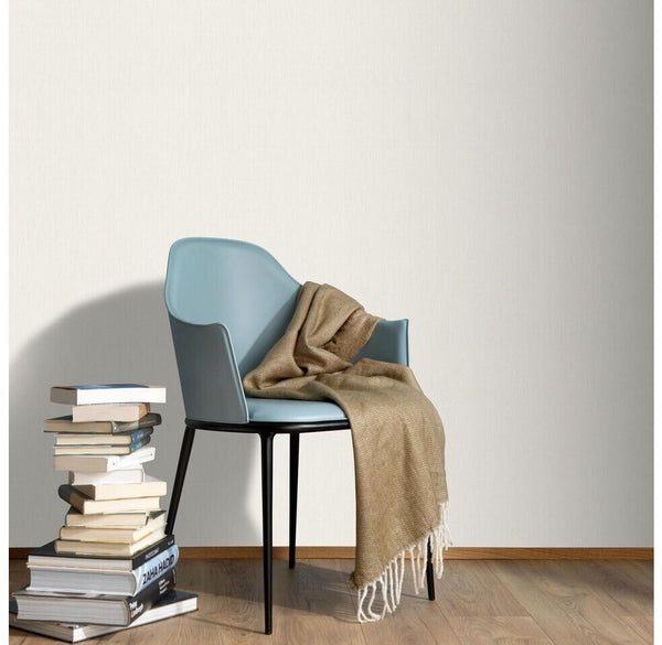 Erismann Fashion For Walls 4 10376-26 wallpaper lounge feature wall behind a modern armchair with draped throw and a stack of books on wooden floor, calm minimalist vibe.