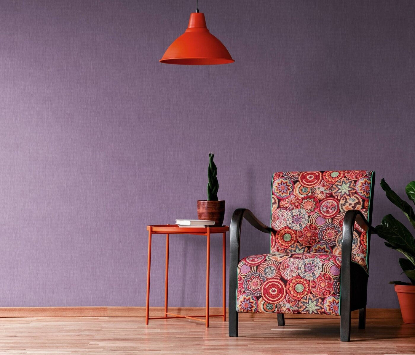 Erismann Fashion For Walls 4 10376-45 wallpaper lounge feature wall in purple behind patterned accent chair, orange side table with potted plant and book, orange pendant light, wood flooring, cozy modern vibe.