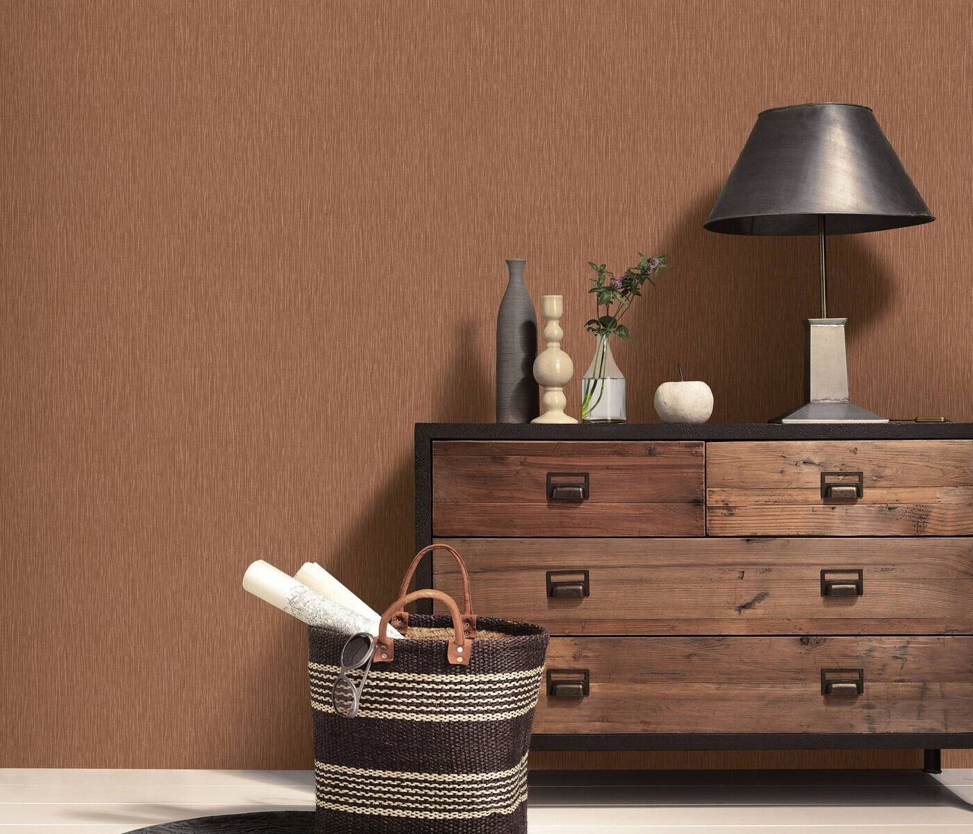 Erismann Fashion For Walls 4 10376-48 wallpaper lounge feature wall behind a rustic wooden sideboard topped with a metal lamp, vases, and a small plant, with a striped woven basket in the foreground for a warm, cozy vibe.