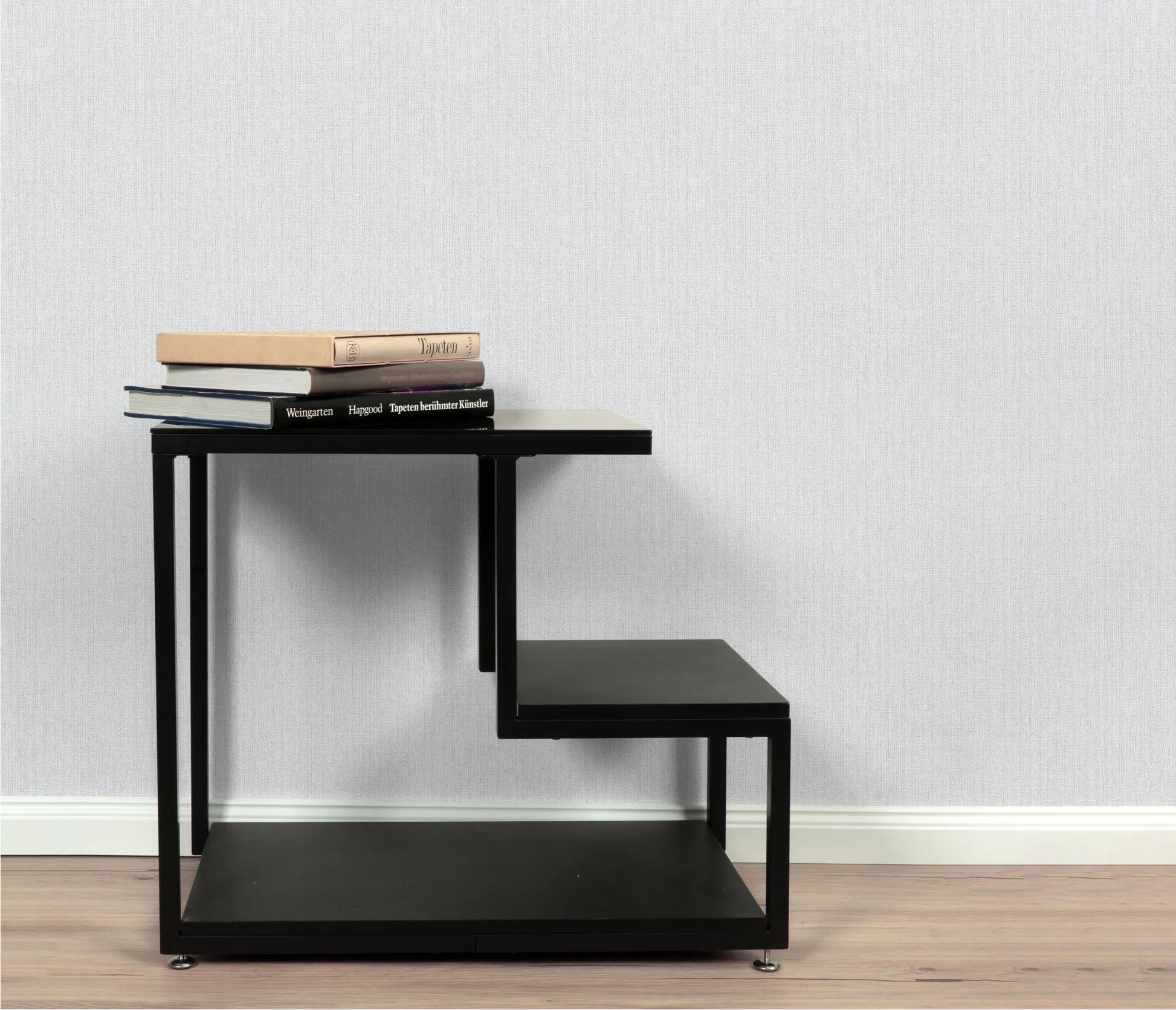Erismann Forest Dreams 10559-10 wallpaper on a pale textured wall behind a black tiered shelf with stacked books.