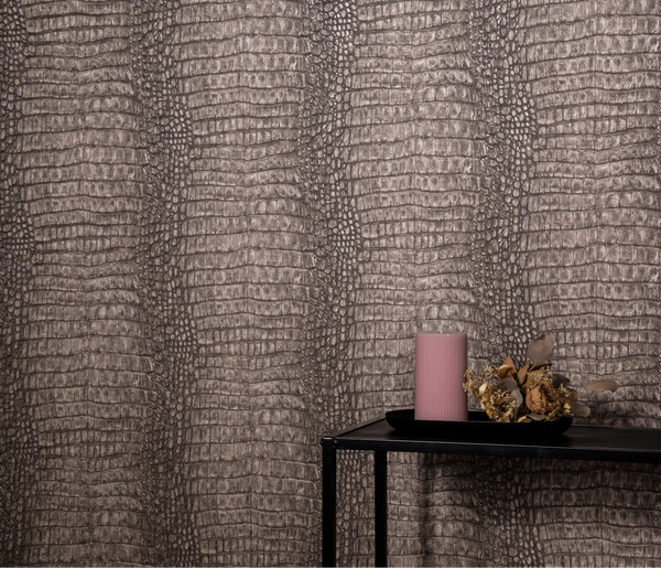 Erismann Forest Dreams 10560-11 wallpaper with reptile-scale textured wall behind a black console table, pink candle, and dried flowers.